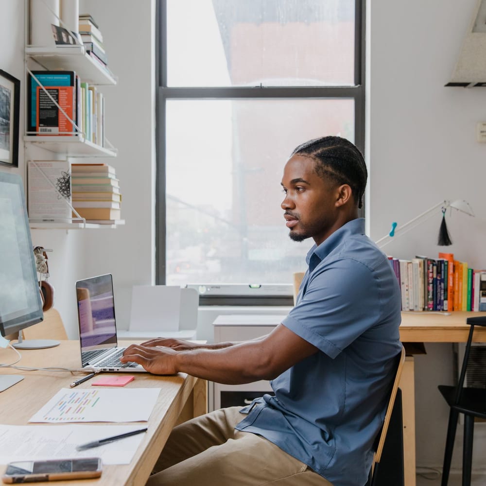 A person working at a desk with two screens, notes and bookshelves